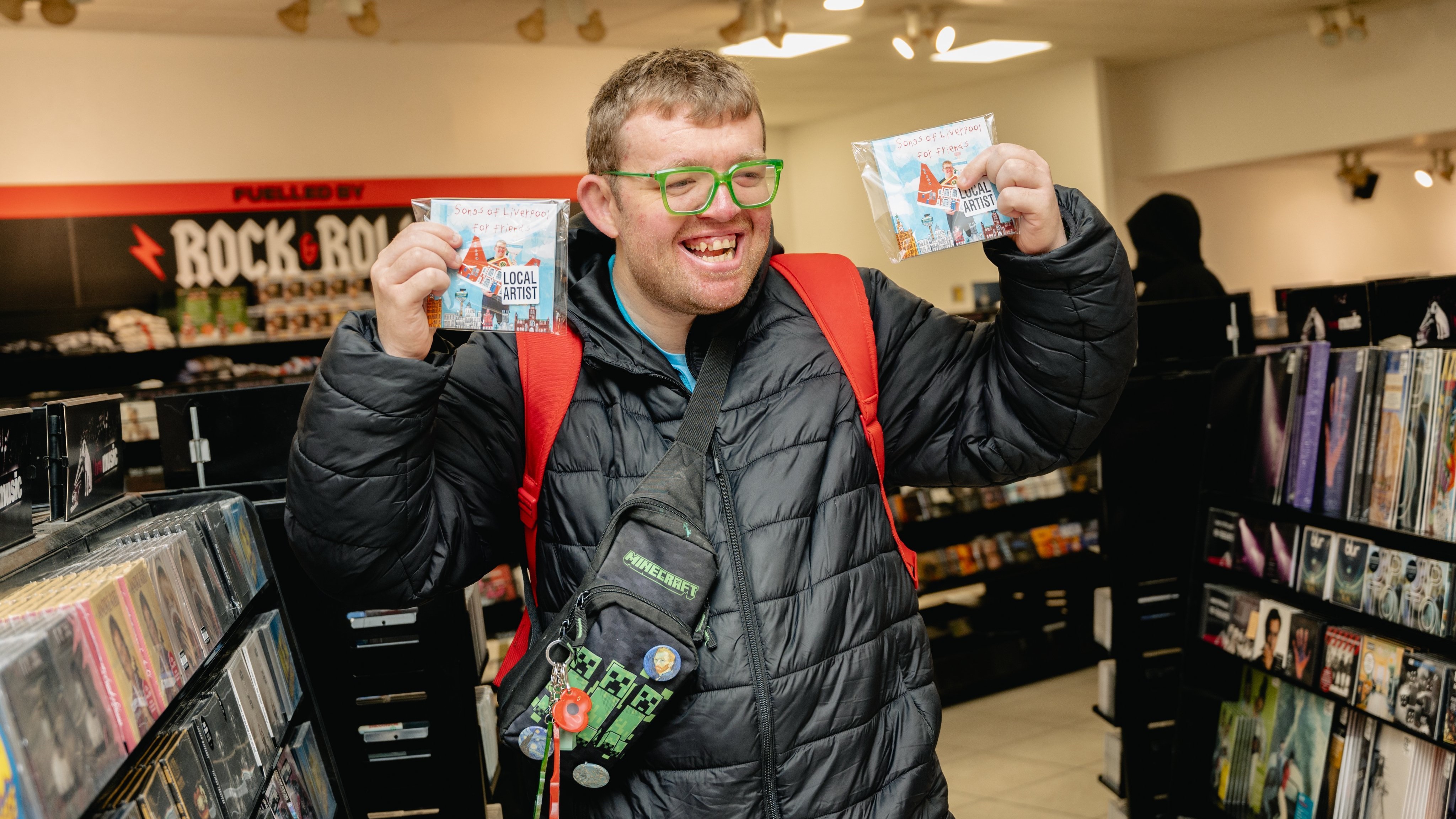 Josh stands in HMV wearing a black coat holding up two of his CD's