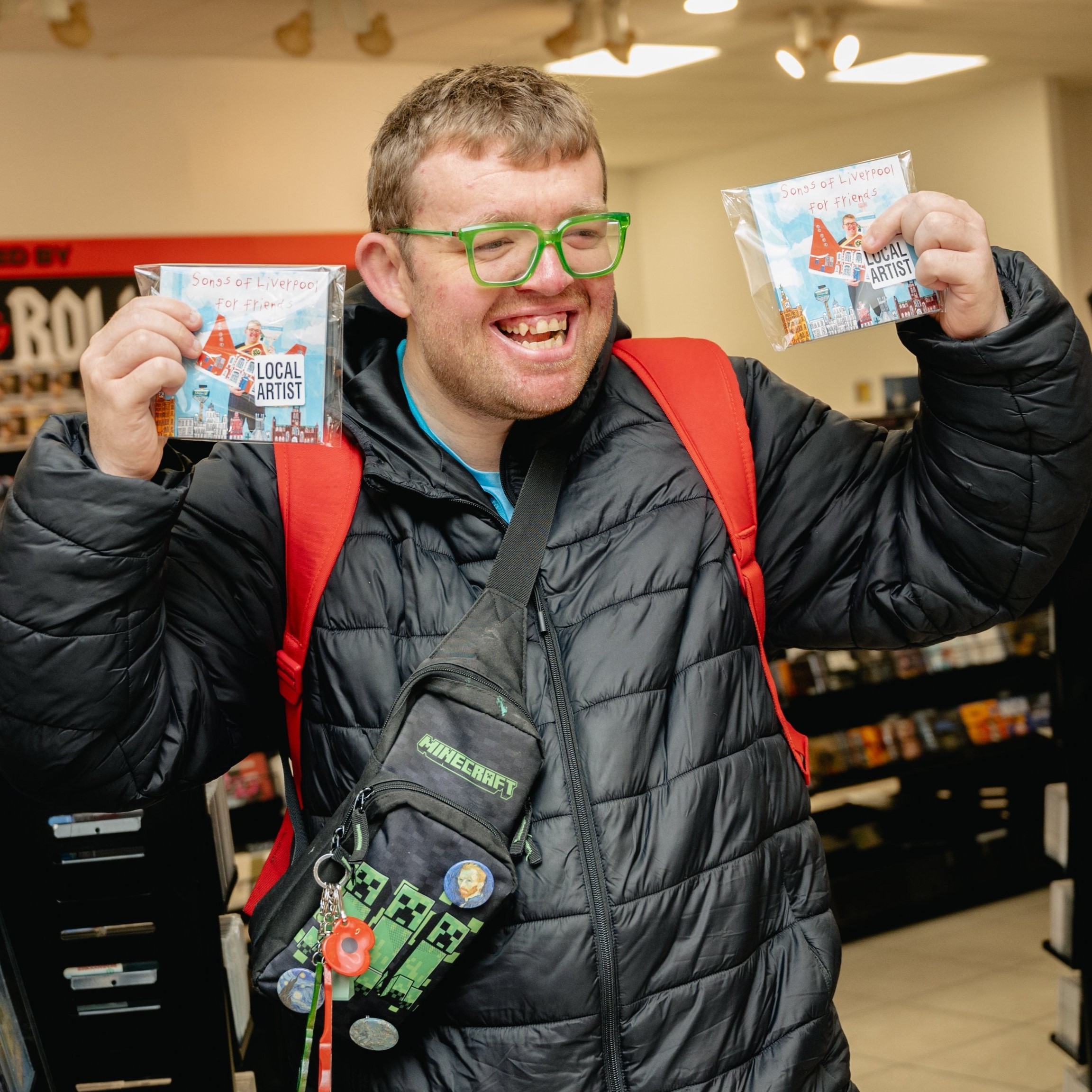 Josh stands in HMV wearing a black coat holding up two of his CD's