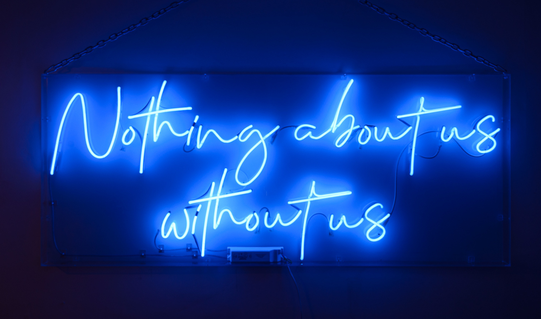 Neon sign reads 'Nothing about us without us' in blue