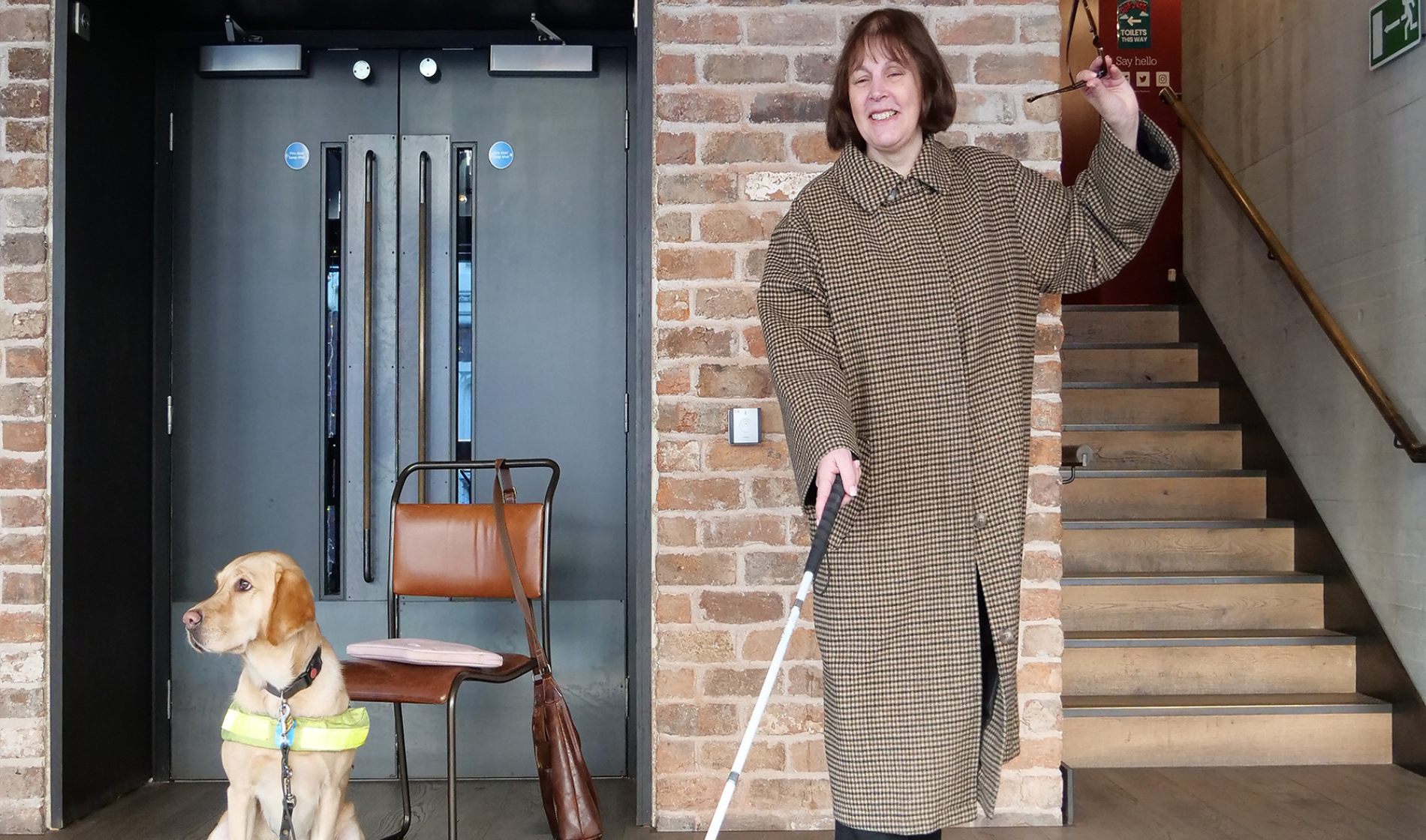 Image of Mandy Redvers-Rowe holding a cane standing next to a guide dog